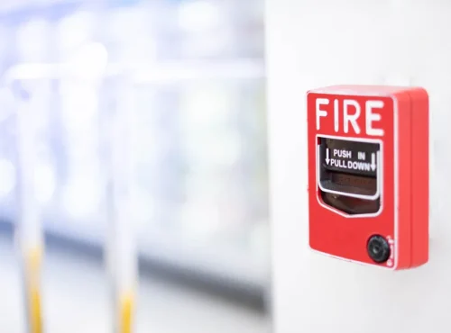 The red fire alarm switch on the white wall at the supermarket.